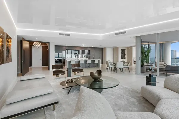 Sala de penthouse con mobiliario blanco y puertas de vidrio hacia un balcón con vista a la ciudad